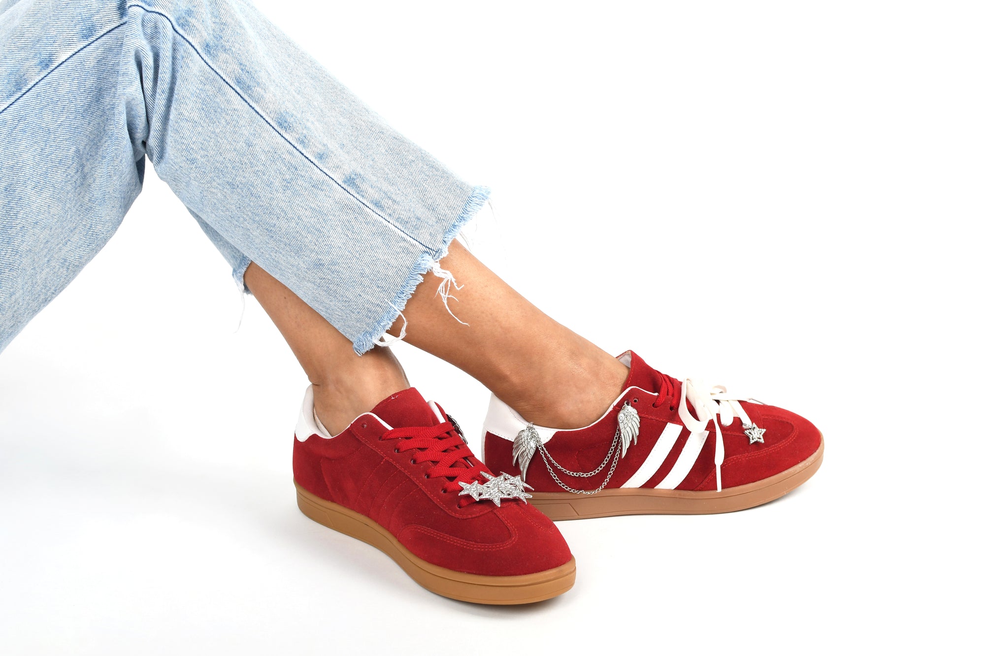 Red sneakers with white accents worn with light blue jeans on a white background