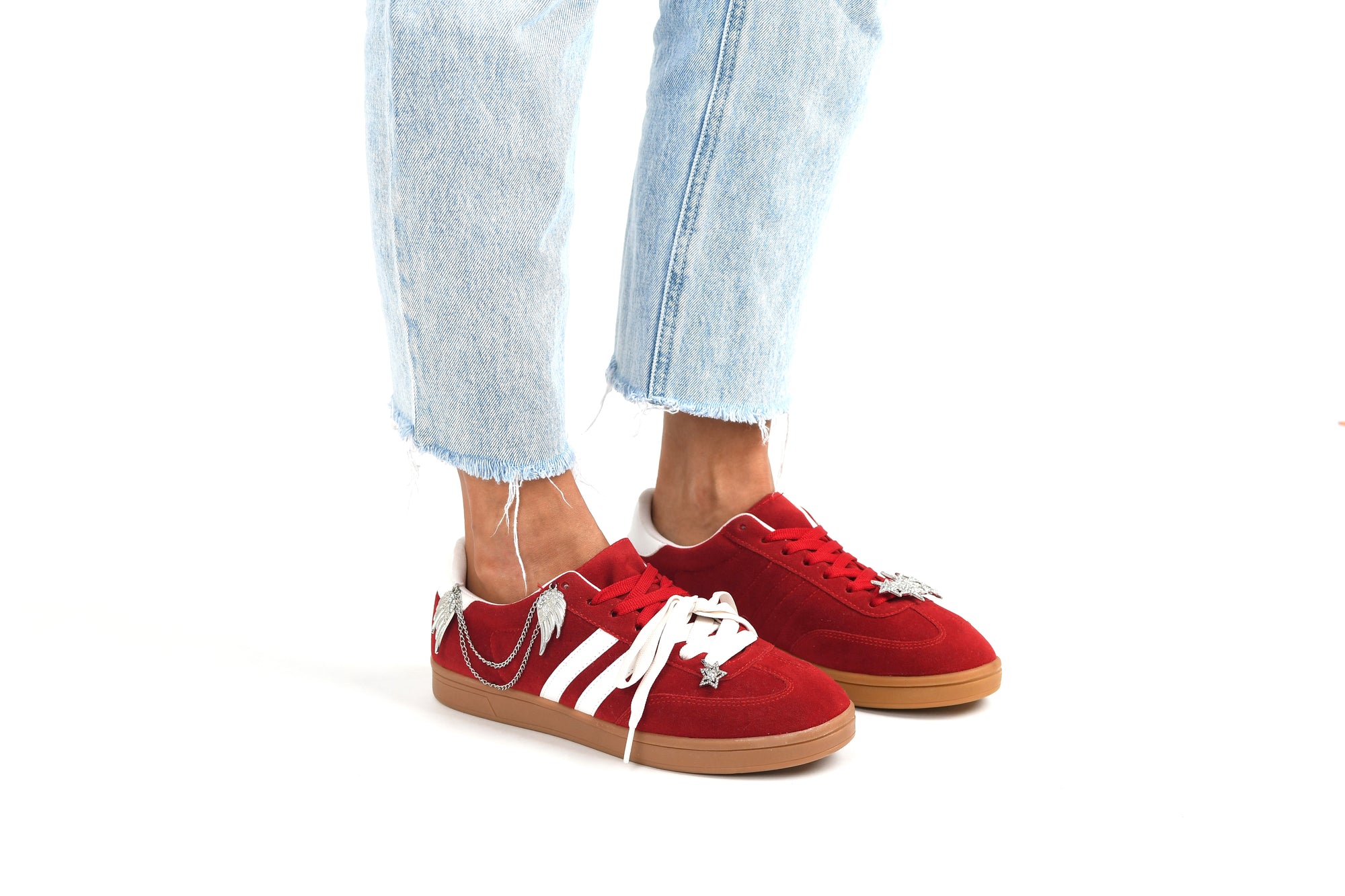 Red sneakers with white laces worn with light blue jeans on a white background